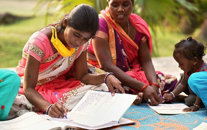 Two women and a girl sitting on blanket; one women writing in a notebook