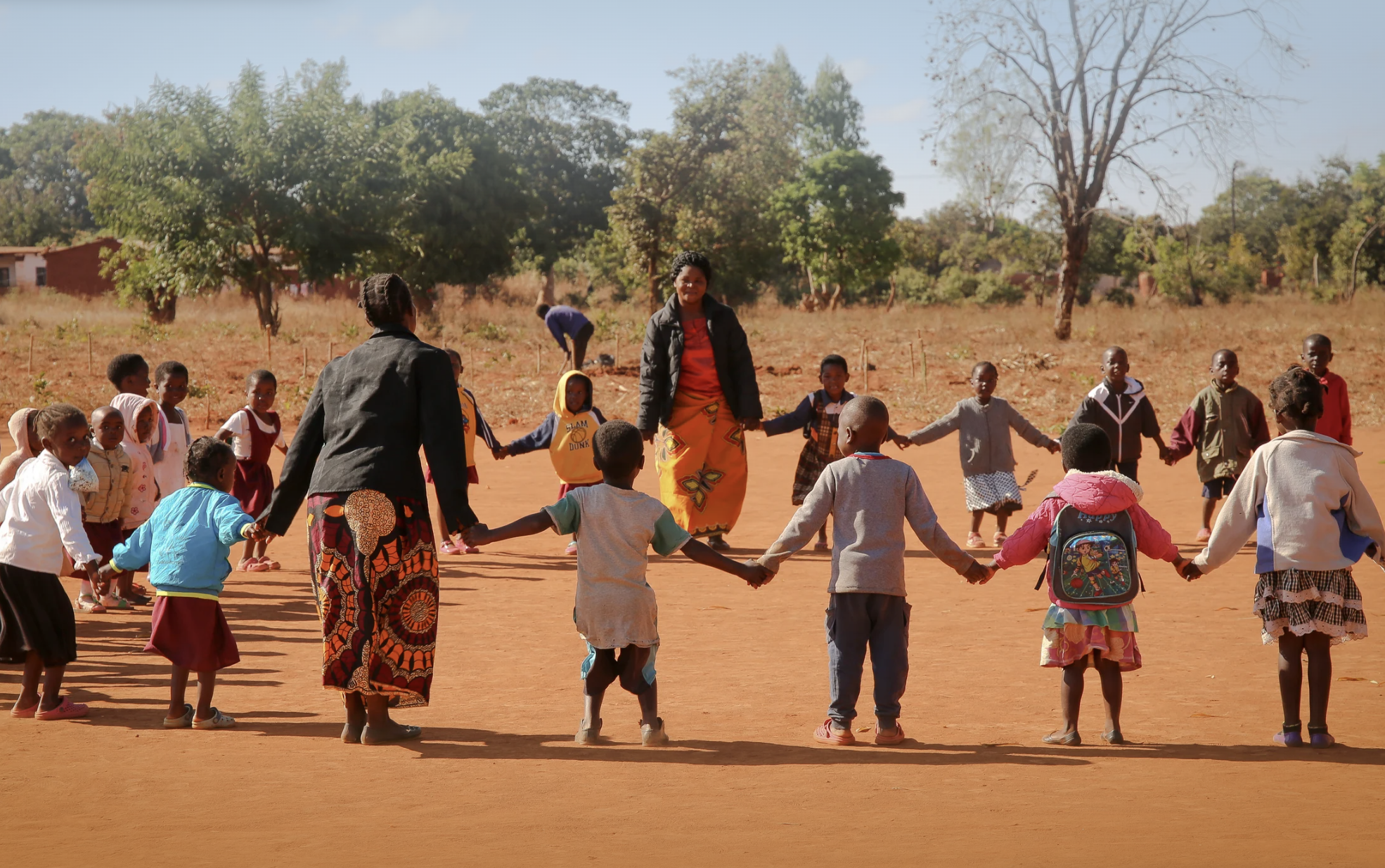 Teachers and children holding hands in a big circle outdoors