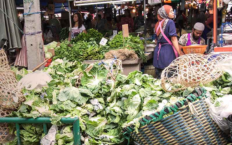 Pile of discarded cabbages and other greens in a market on left front, woman and vendor right rear