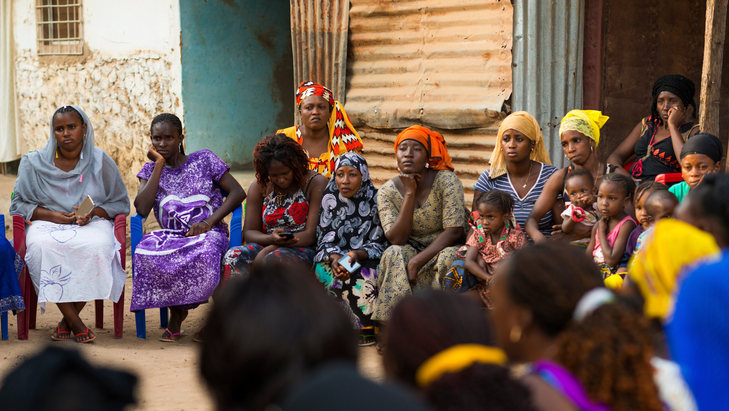 Women with children sitting in a circle outside a building.