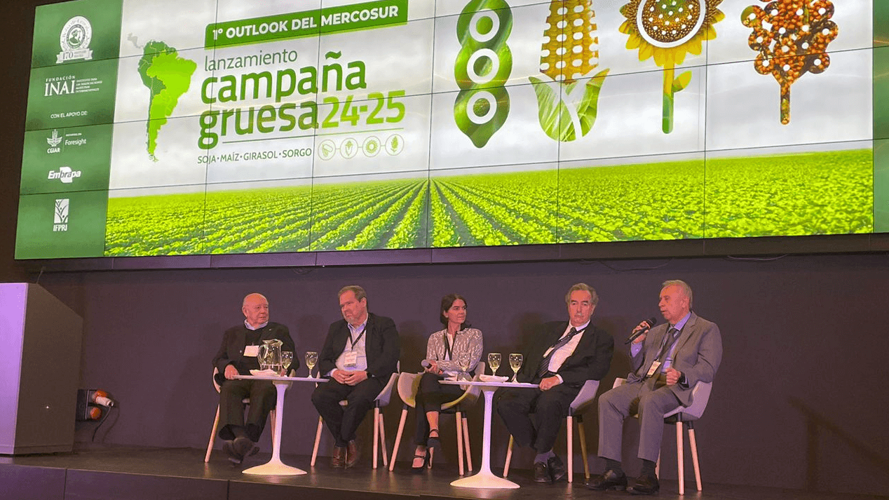 Panelists sitting on stage under screen showing event title and sponsors