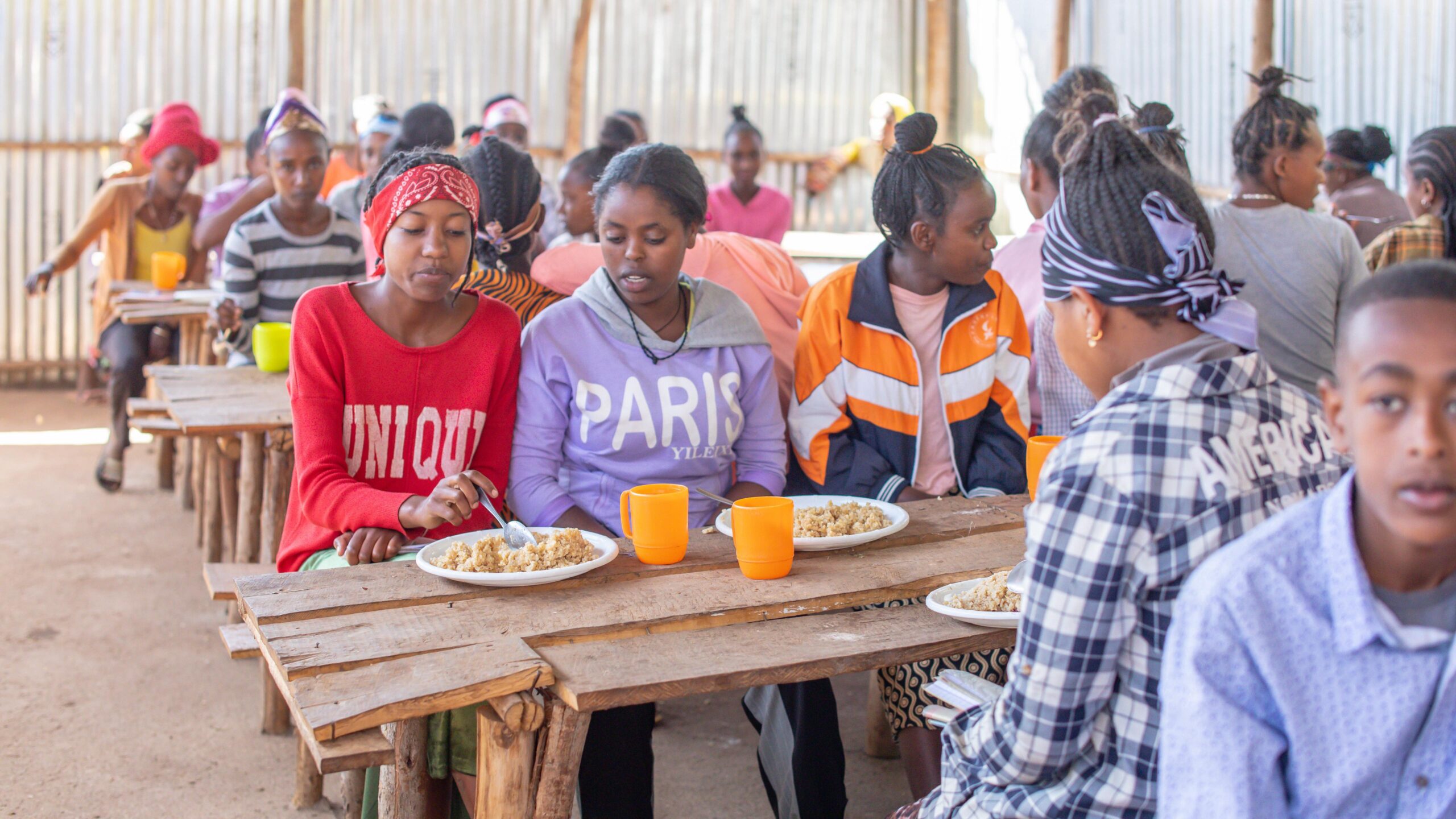 High school students sit at wooden tables eating a rice dish