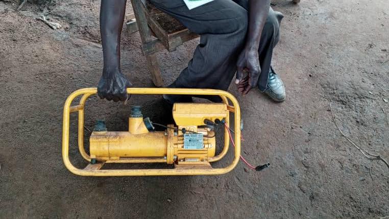 Man holds yellow pump apparatus, hands and lower body visible.