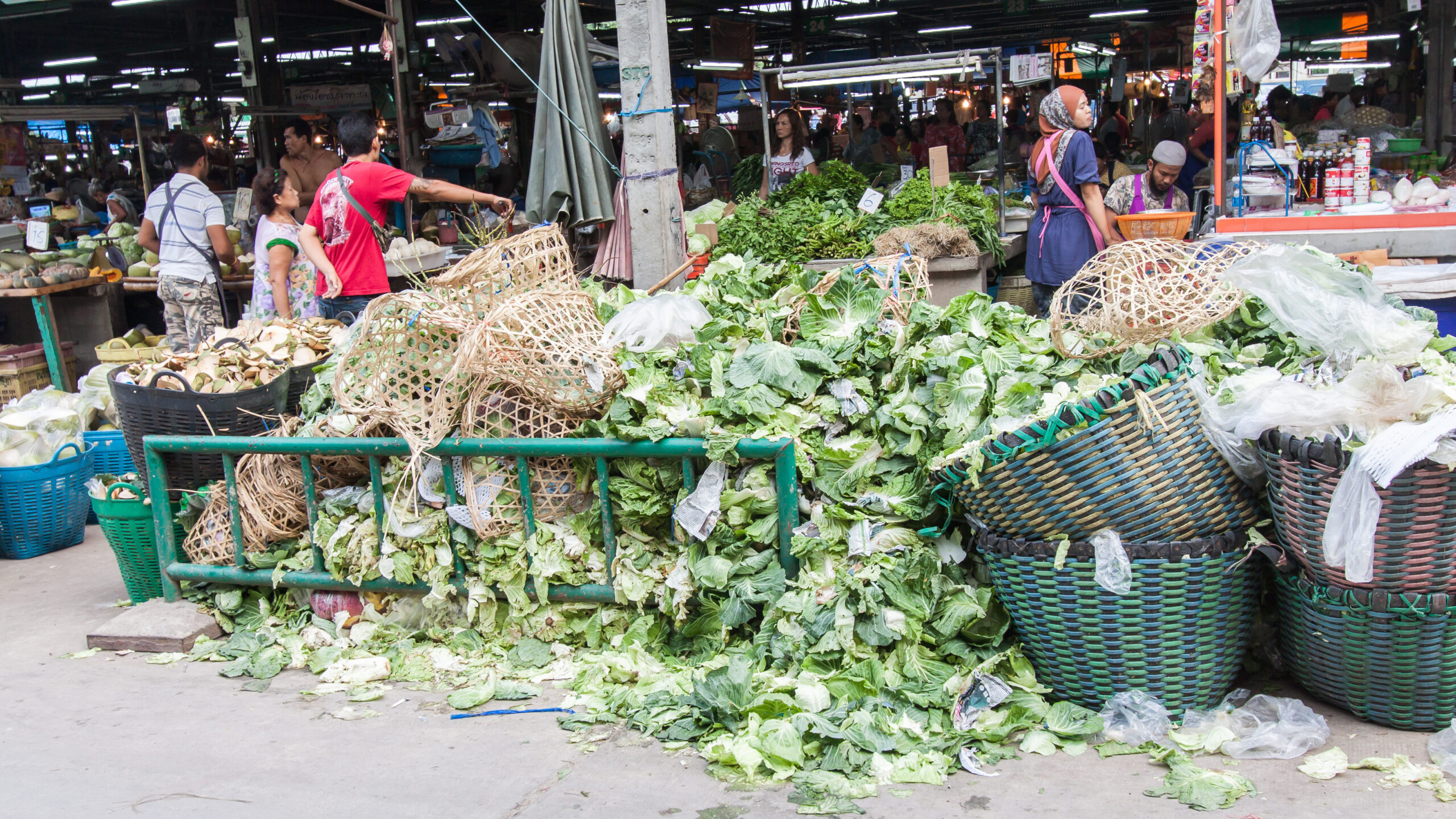 Pile of discarded cabbages among baskets outside food market, people and market interior in background