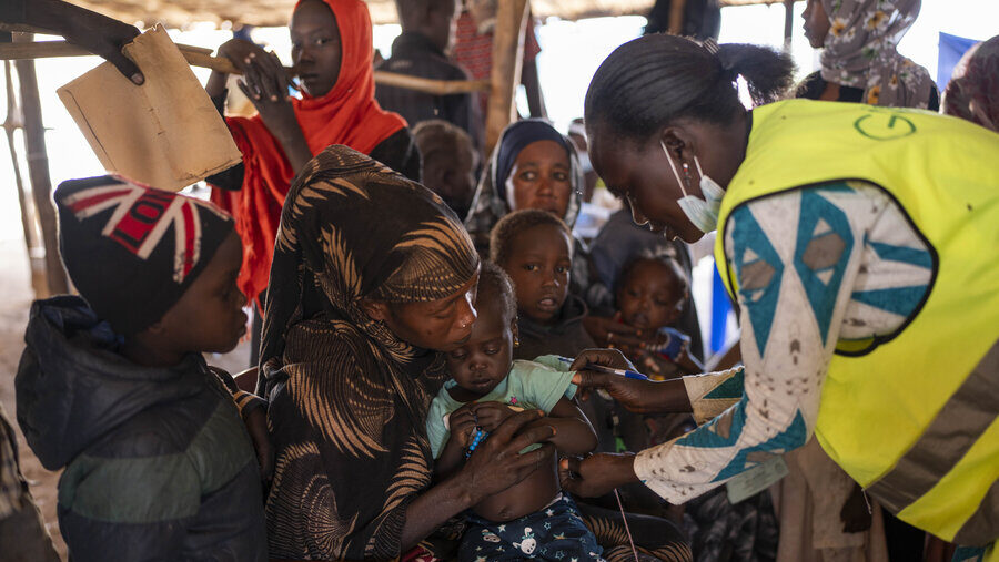 Woman, right, examines small child in arms of mother; other women and children surrounding them