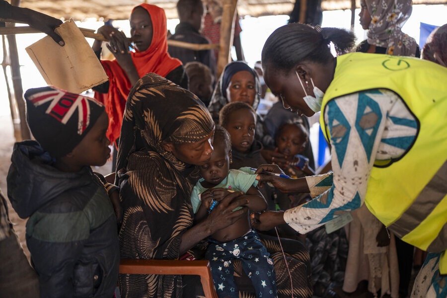 Woman, right, examines small child in arms of mother; other women and children surrounding them