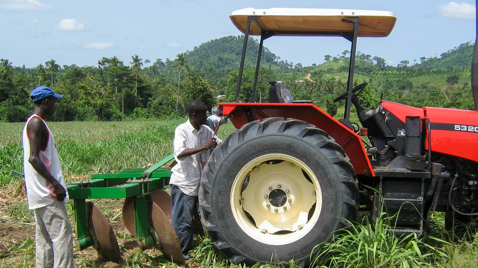 Man standing, left, other man next to red tractor, attaching implement.